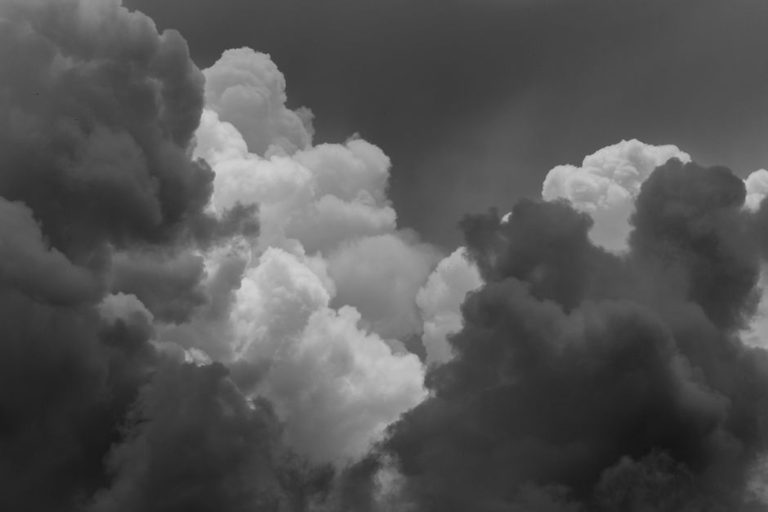 Dark storm clouds with dense, towering formations and bright patches in the center, creating a dramatic, monochrome sky.